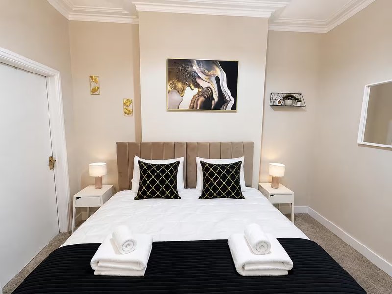 Modern bedroom with upholstered headboard, white bedding, black runner, and wall art