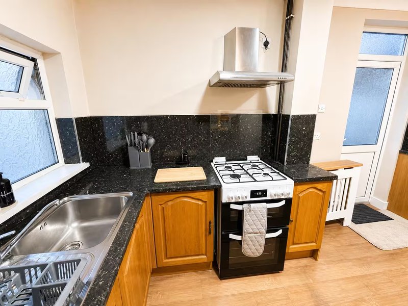 Kitchen with wooden cabinets, black granite countertop, stainless steel sink and cooker hood