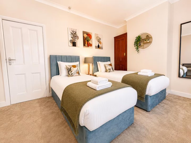 Twin bedroom with blue upholstered beds, white pillows, olive throws, and wall art
