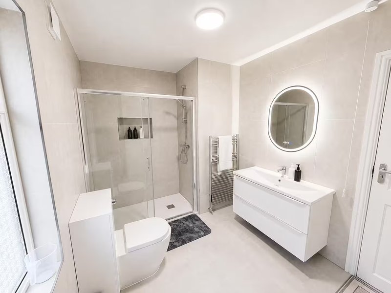 Modern bathroom with walk-in shower, white vanity, illuminated mirror and heated towel rail
