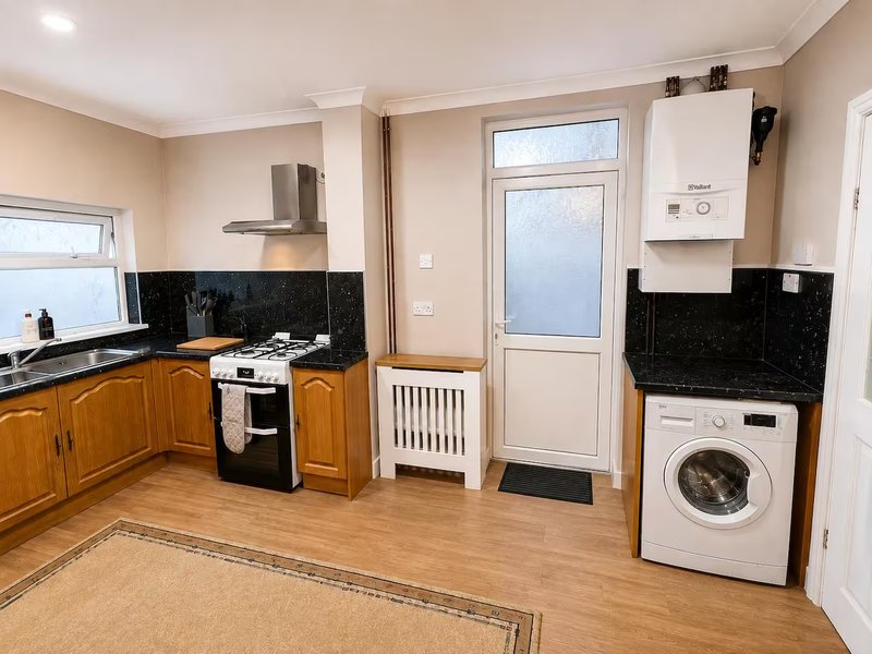 Kitchen and laundry area with wooden cabinets, black countertops, washing machine and appliances
