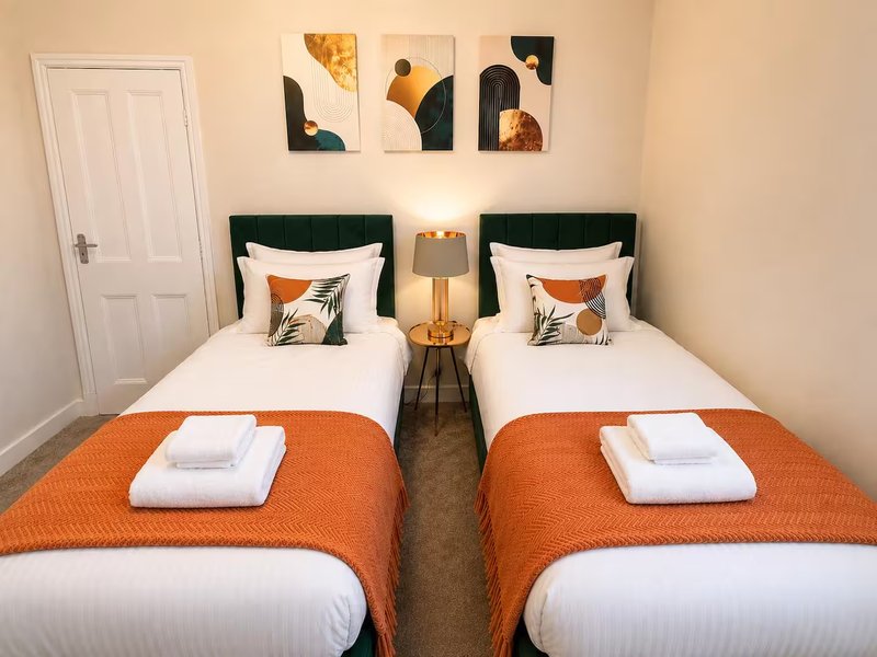 Twin bedroom with orange throws, white pillows, green headboards and wall art