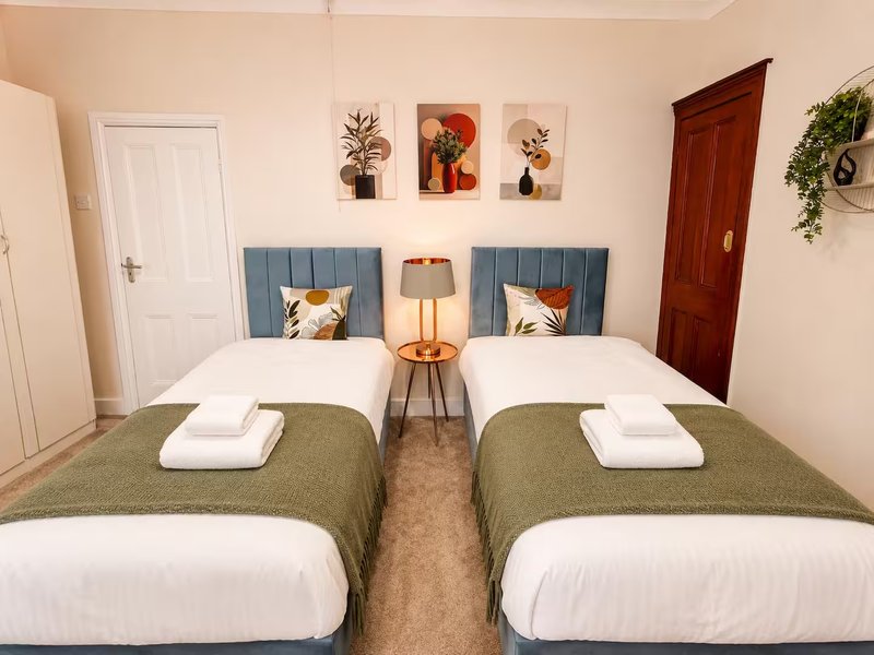 Twin bedroom with two beds, blue headboards, side table lamp, wall art and doors