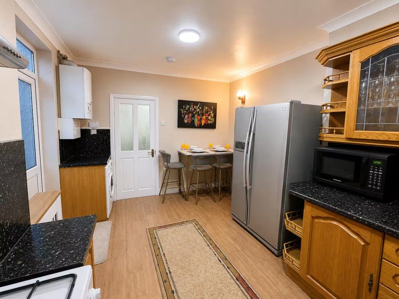 Modern kitchen with stainless steel refrigerator, black granite countertops, wooden cabinetry and breakfast bar
