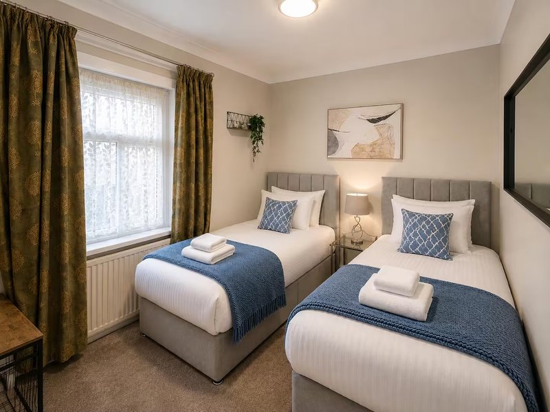 Twin bedroom with two single beds, grey headboards, blue throws and patterned cushions, natural light from window