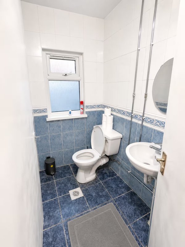 Compact bathroom with blue tile flooring, white walls, toilet, sink and window