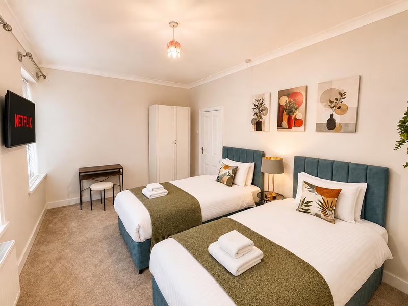 Twin bedroom with two beds, teal headboards, wall art, TV, and pendant lighting