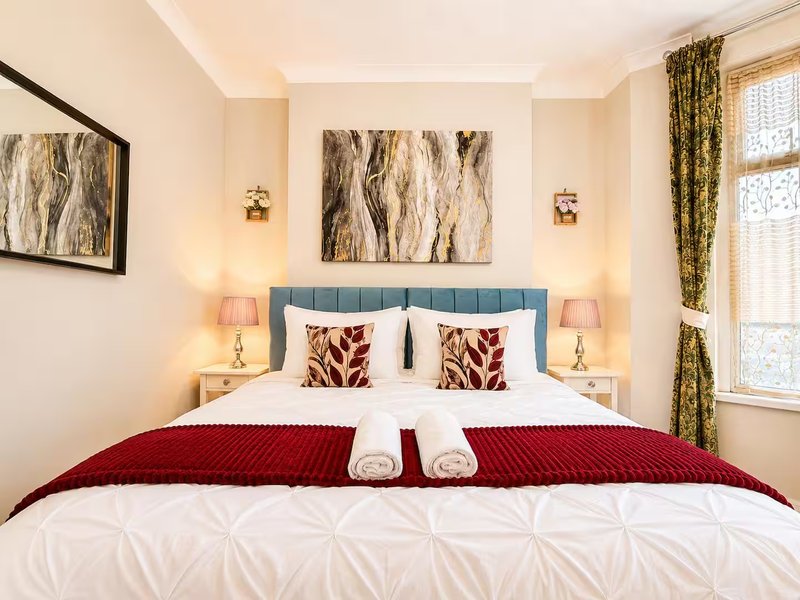 Bedroom with blue upholstered bed, white bedding, red throw, decorative pillows and wall art