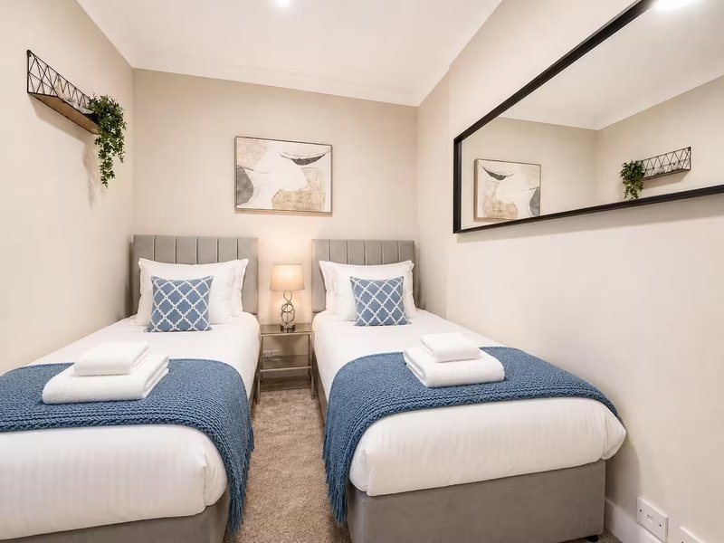 Twin bedroom with two single beds, blue bedding, white pillows, and minimalist wall decor