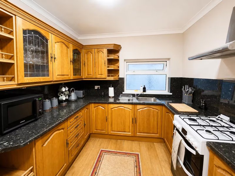 Spacious kitchen with wooden cabinets, black granite countertop, gas range and window