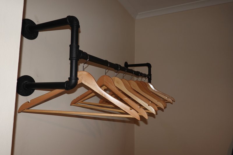 Wall-mounted black pipe clothing rack with wooden hangers in bedroom corner