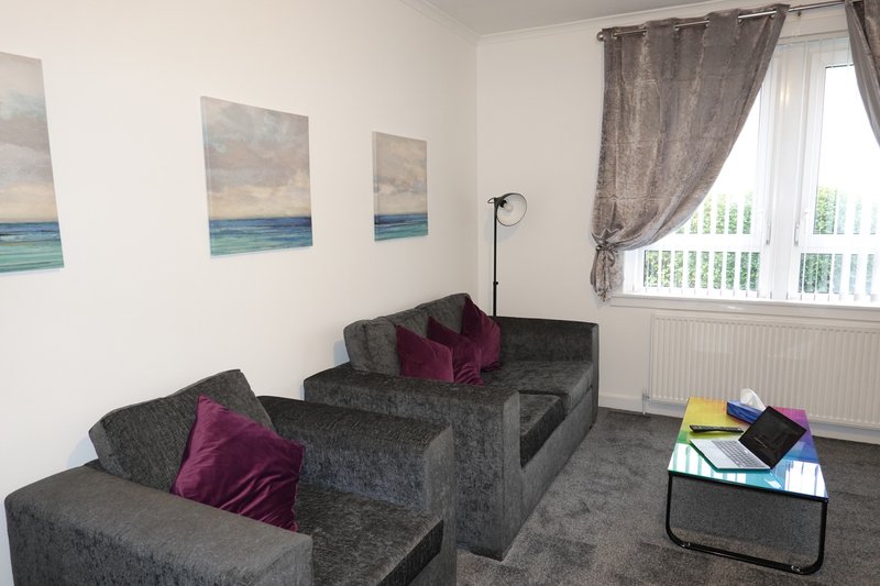 Living room with two grey sofas, burgundy cushions, abstract seascape wall art, floor lamp and window with grey curtains