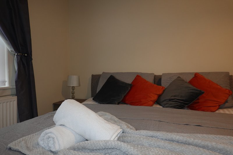 Bedroom with double bed, rolled towels, red and black cushions, bedside lamp and window.