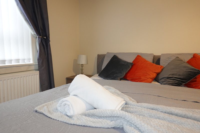 Bedroom with double bed, rolled towels, decorative pillows and window with curtains