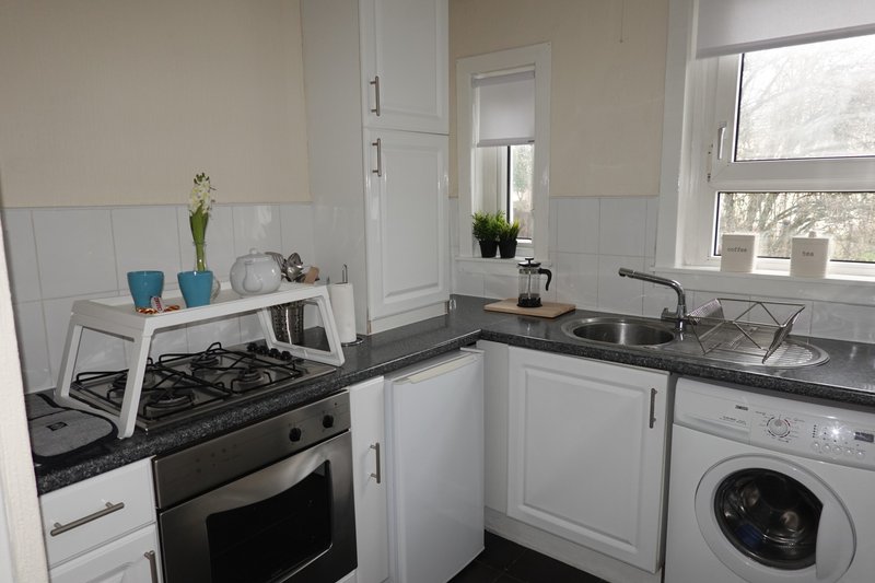 Modern white kitchen with black countertops, gas stove, washing machine and window view