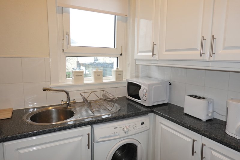 Small white kitchen with sink, washing machine, microwave and dark countertops