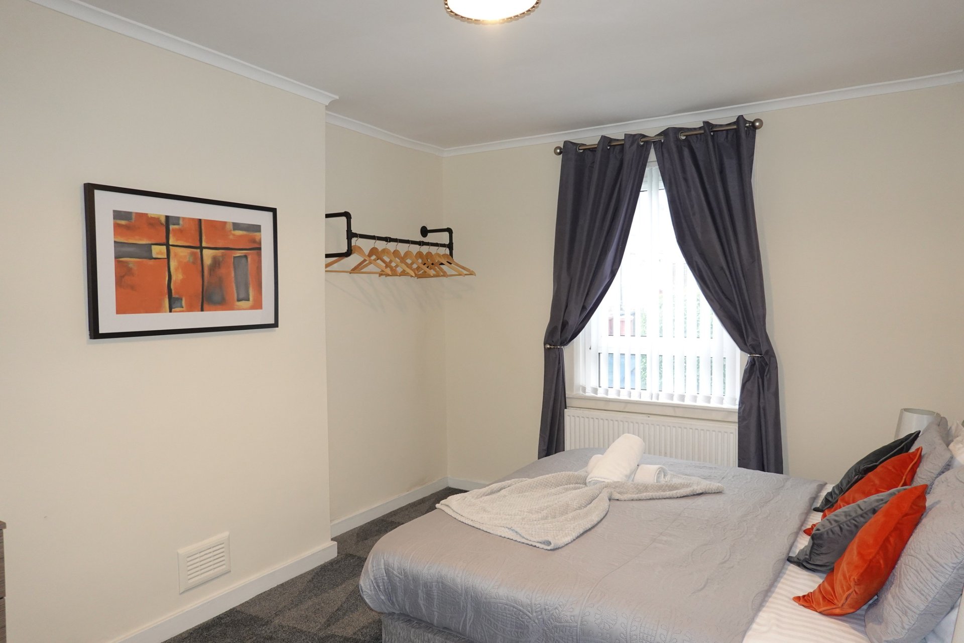 Bedroom with double bed, dark curtains, framed wall art, and wooden shelf
