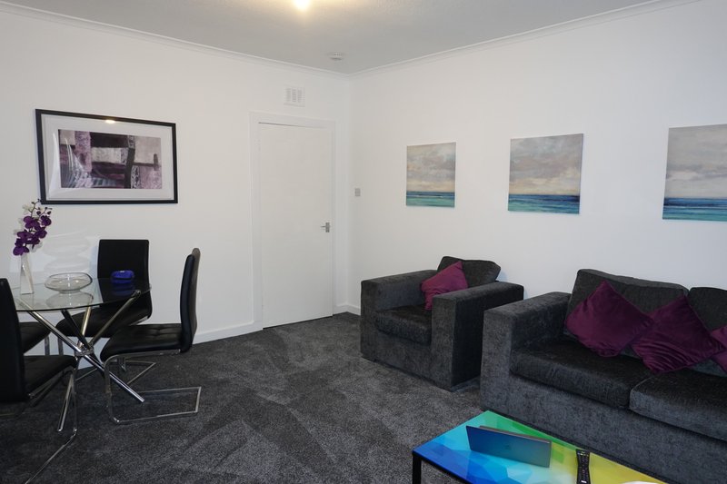Modern living room with dark sofas, dining table, framed artwork and seascape paintings