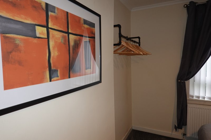 Bedroom with framed abstract artwork, coat rack, black curtains and radiator