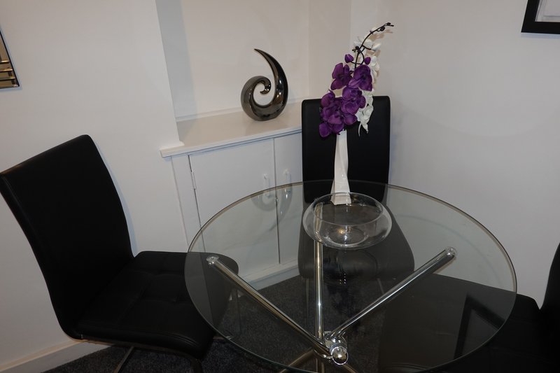 Modern dining area with round glass table, black chair, and purple floral centerpiece