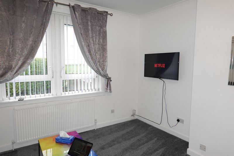Bedroom with wall-mounted TV, grey carpet, window with curtains and radiator