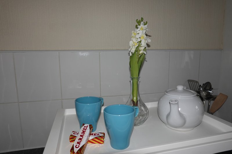 Kitchen counter with white tile backsplash, blue mugs, vase with white flowers, and teapot