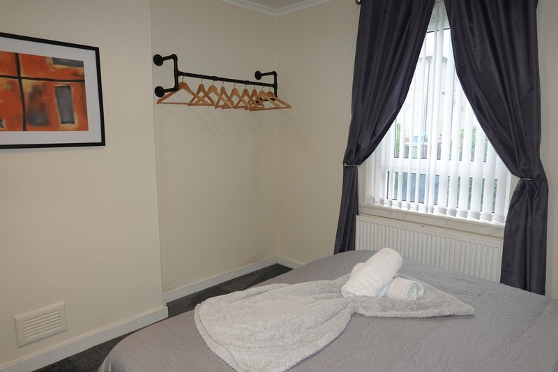 Bedroom with double bed, white pillows, grey bedding, dark curtains and window.