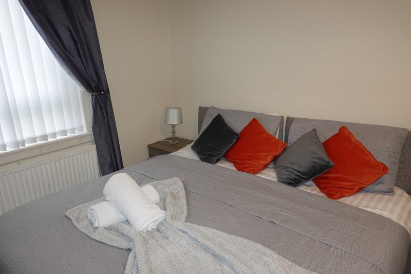 Bedroom with double bed, red and black cushions, white towels, and bedside lamp