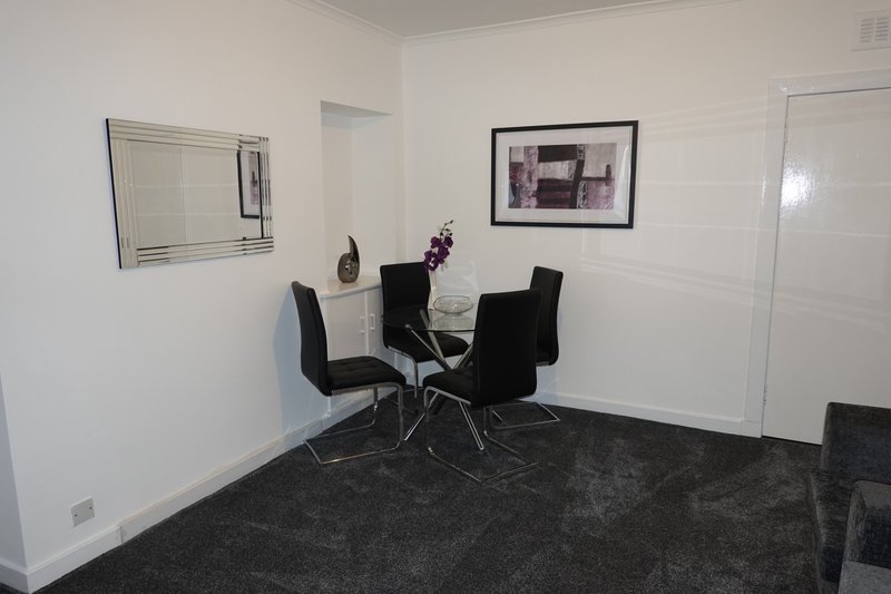 Modern dining room with round glass table, black chairs, and grey carpet flooring