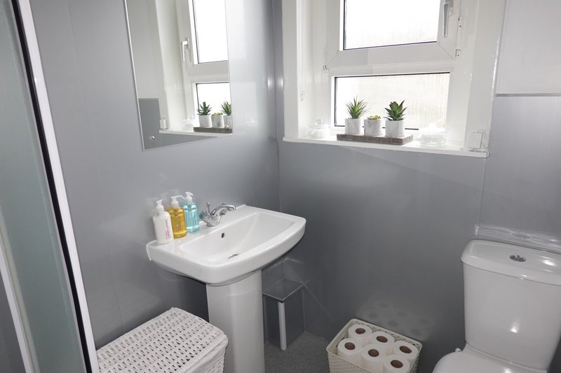Small bathroom with pedestal sink, toilet, and window with potted plants