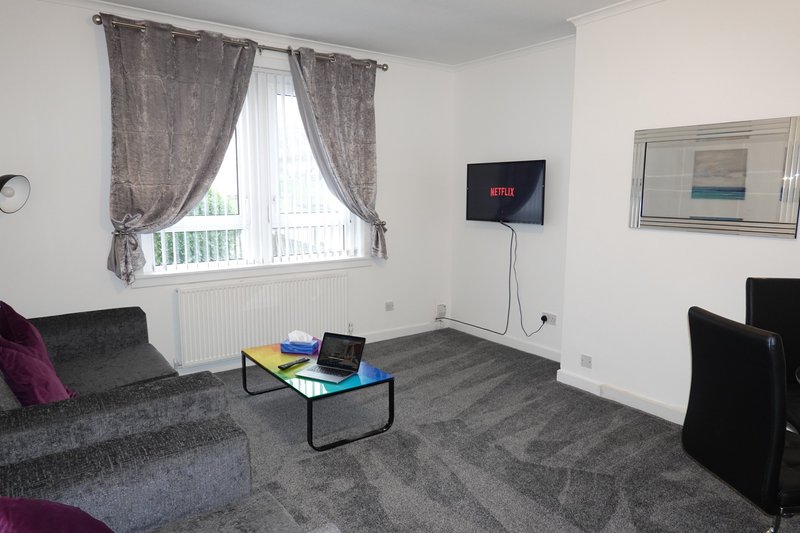 Living room with gray sofa, wall-mounted TV, coffee table, and large window with gray curtains
