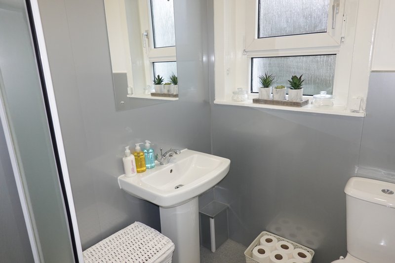 Bathroom with pedestal sink, toilet, small windows and toiletries on shelves