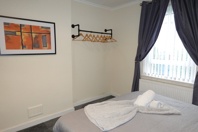 Bedroom with double bed, white pillows, dark curtains, wall art and wooden coat rack