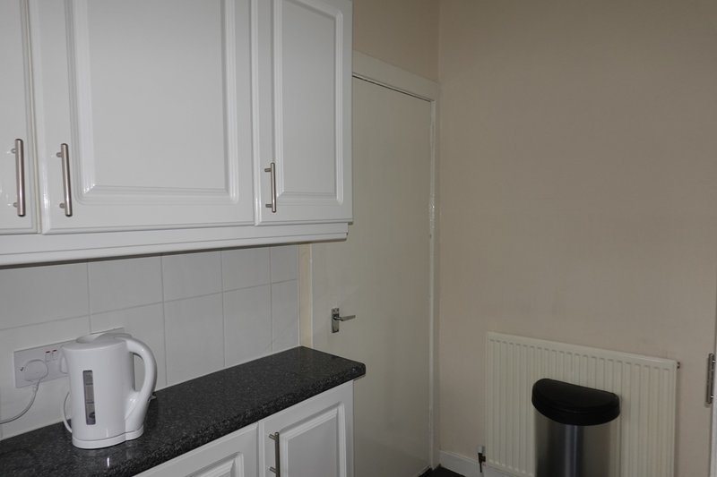 Kitchen area with white cabinetry, black countertop, kettle and waste bin