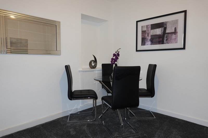 Modern dining area with black table, four chairs, white walls and framed artwork