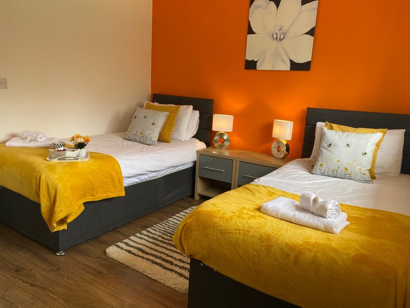 Twin bedroom with yellow blankets, orange accent wall, bedside lamps and wall art