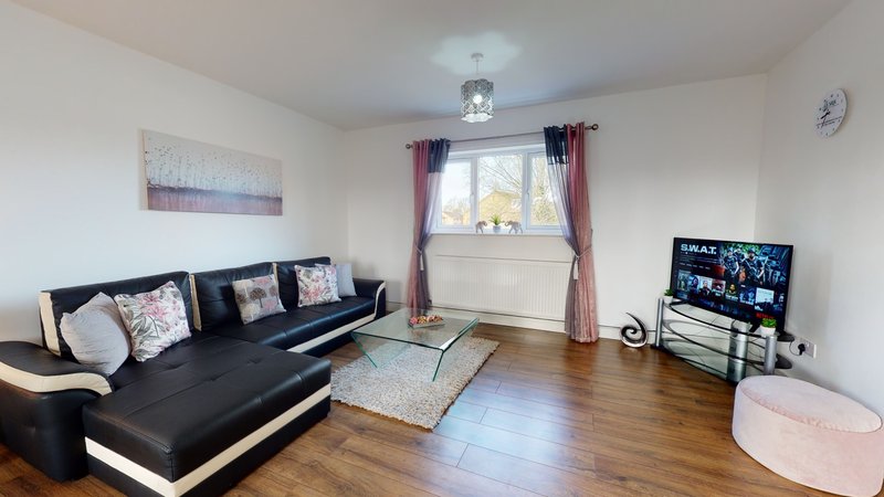 Spacious living room with black sectional sofa, wooden floor, TV, and purple curtains