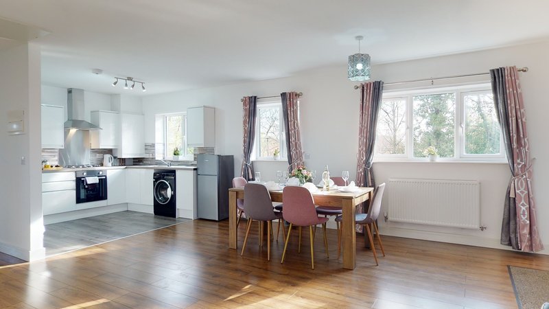 Open-plan kitchen and dining area with wooden flooring, dining table with chairs, and large windows