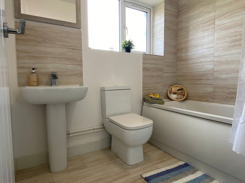 Modern bathroom with pedestal sink, toilet, bathtub, wooden-look tiles and window