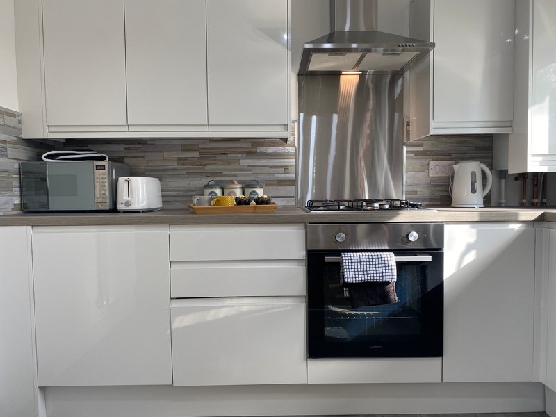 Modern white kitchen with stainless steel range hood, built-in oven, and countertop appliances