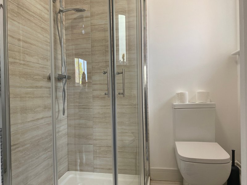 Modern bathroom with walk-in shower, toilet, and neutral tile walls