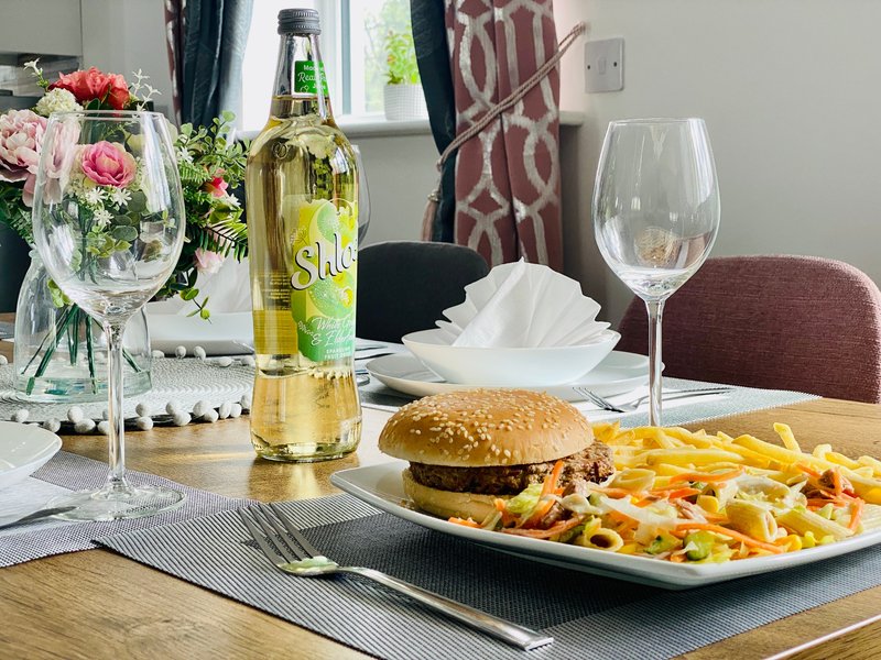 Dining table set with burger, fries, wine bottle, flowers and glassware