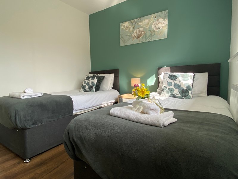 Bedroom with two beds, green accent wall, bedside lamp and framed artwork