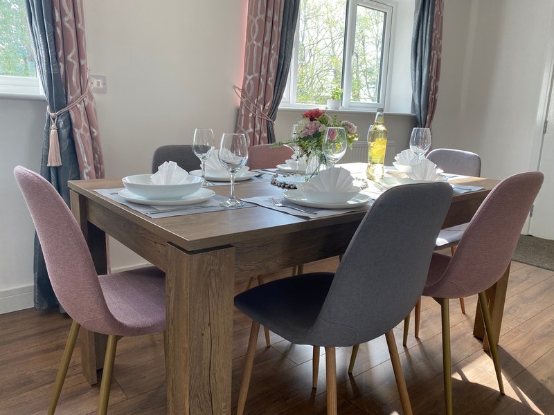 Dining room with wooden table, upholstered chairs, place settings, and flowers by window