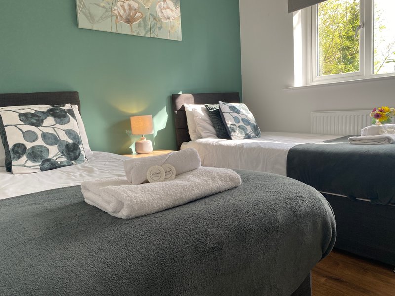 Bedroom with two beds, green walls, rolled towels, decorative pillows and window