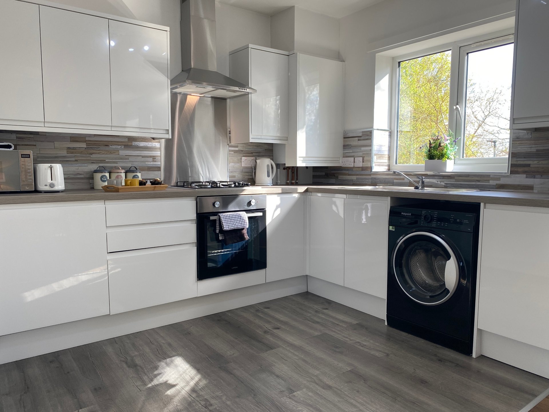 Modern kitchen with white cabinetry, black countertops, stainless steel appliances and large windows