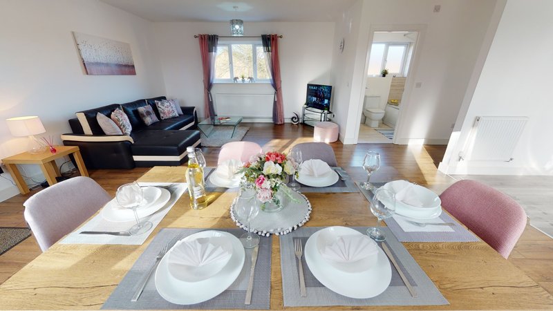 Open-plan living and dining area with wooden table, place settings, floral centerpiece and seating area beyond