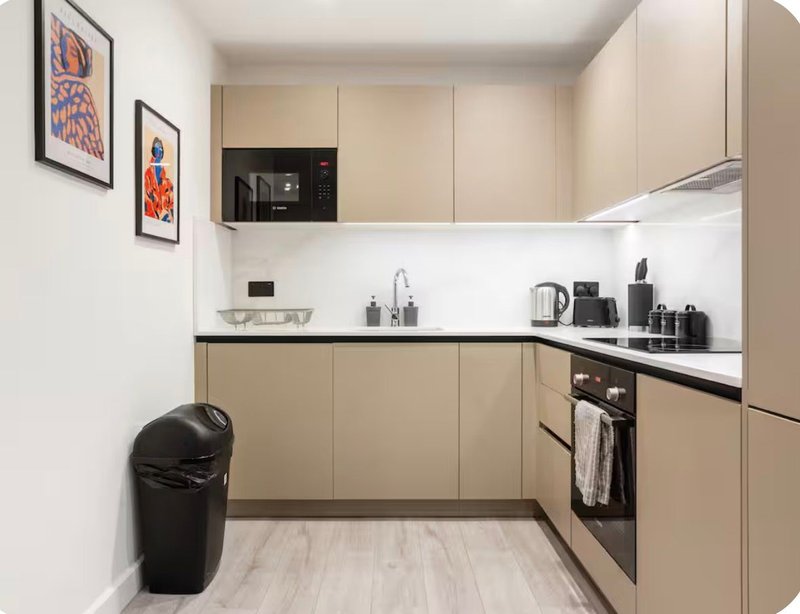 Modern kitchen with beige cabinetry, black appliances, white countertop and framed artwork