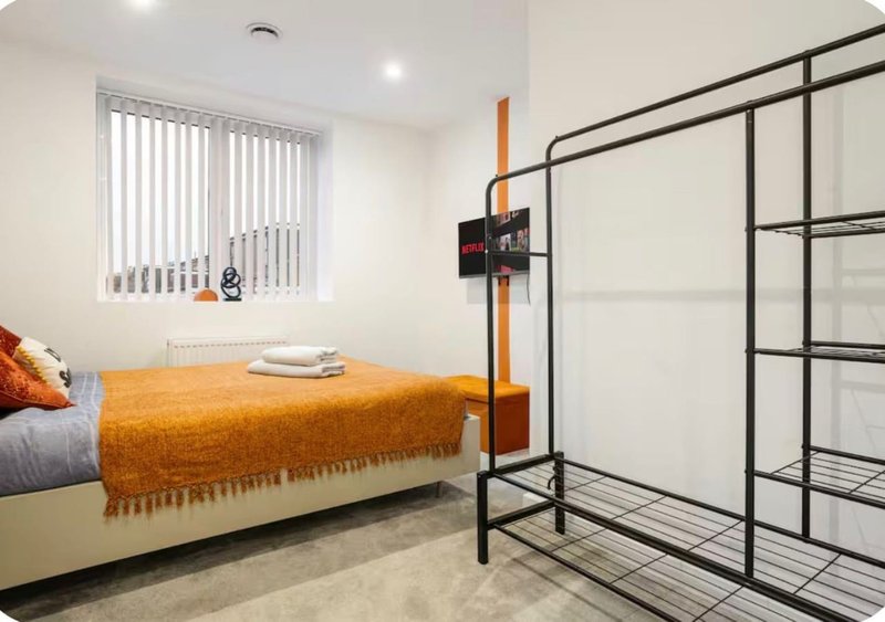 Bedroom with single bed, orange throw blanket, metal bed frame, and vertical blinds