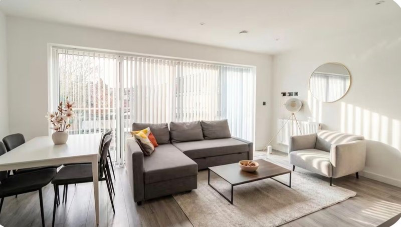 Bright open-plan living room with grey sofa, dining table, armchair and large windows